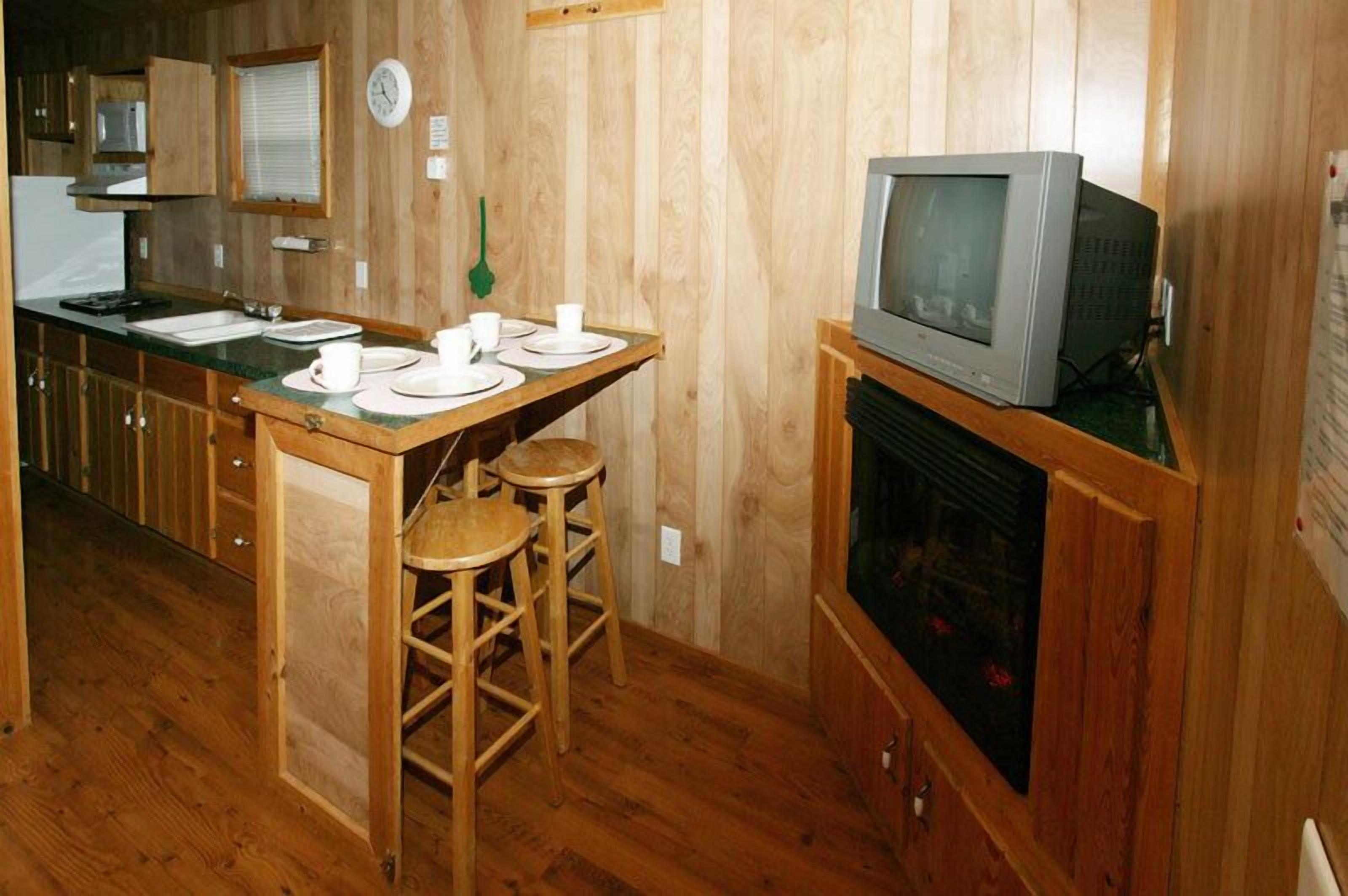A compact kitchen with wooden cabinets, a sink, a stove, and a television on a stand.