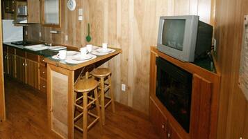 A compact kitchen with wooden cabinets, a sink, a stove, and a television on a stand.
