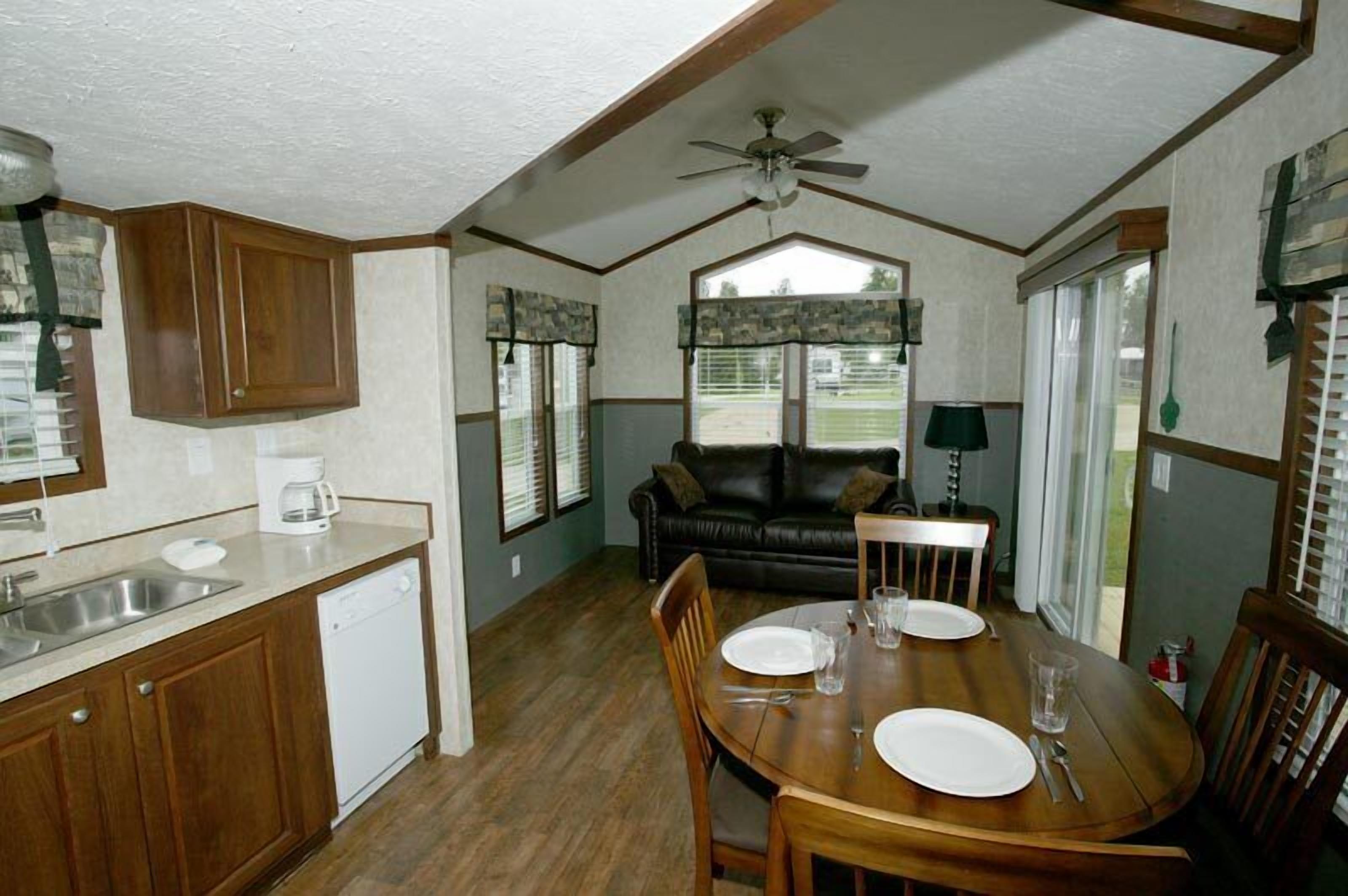A compact kitchen with a dishwasher, a dining table set for four, and a ceiling fan.