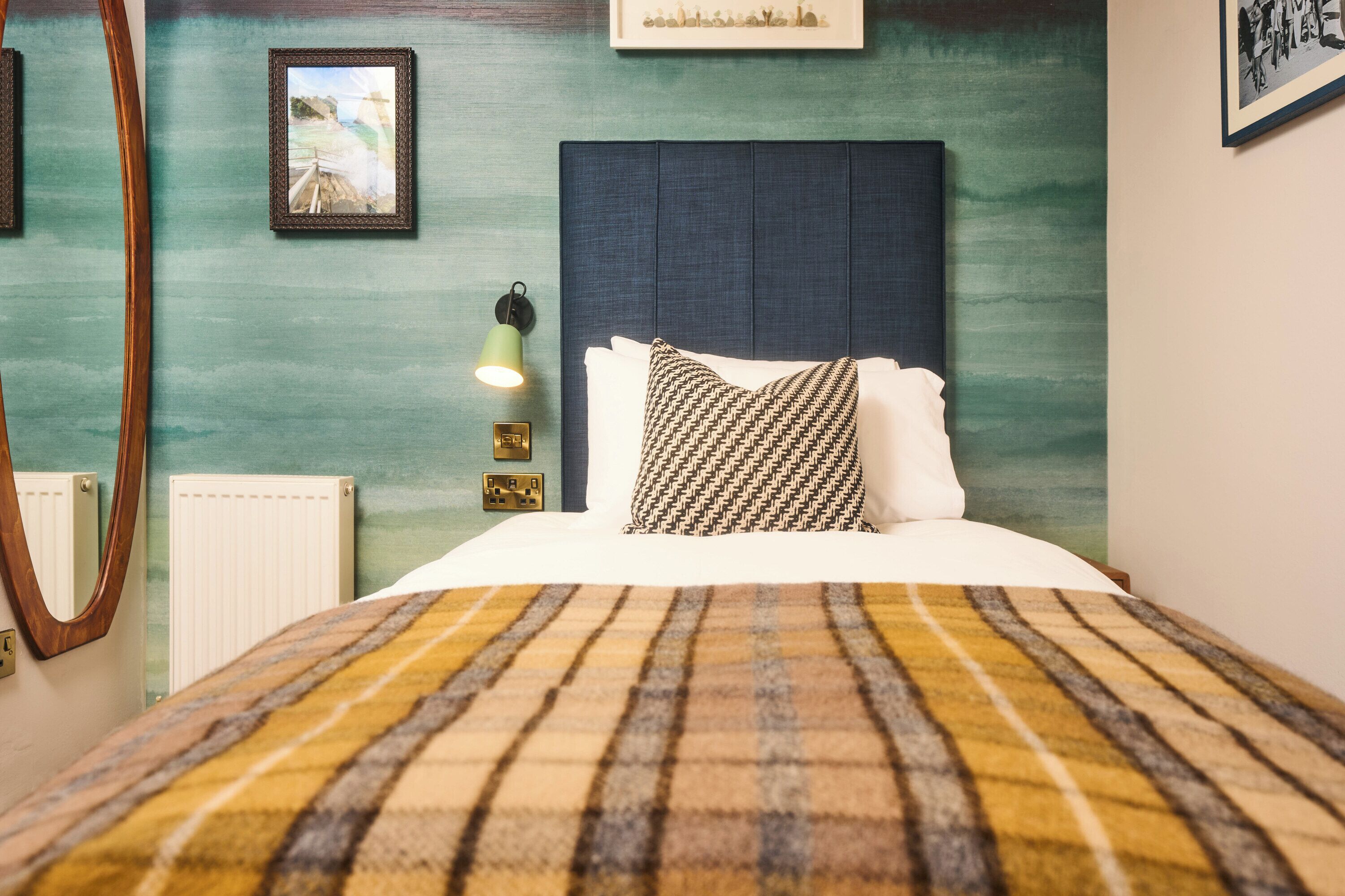 A neatly made bed with a plaid blanket, a headboard, and a wall-mounted light fixture.