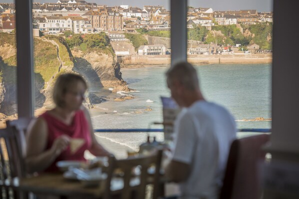 A coastal view with a dining area overlooking the sea and a town in the background. - Great Western Hotel (Newquay)