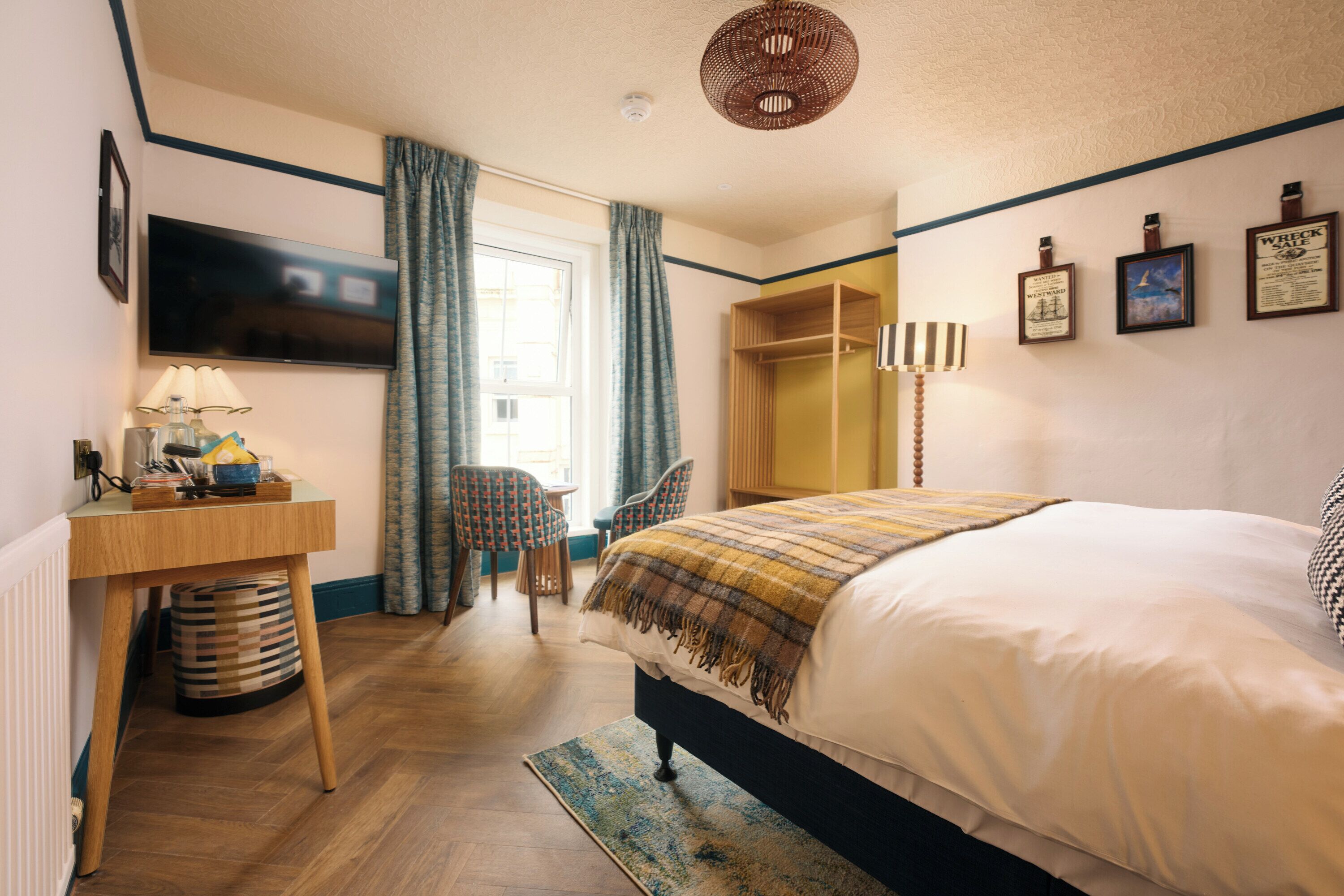 A bedroom with a bed, a desk, a chair, a television, and a window with curtains.
