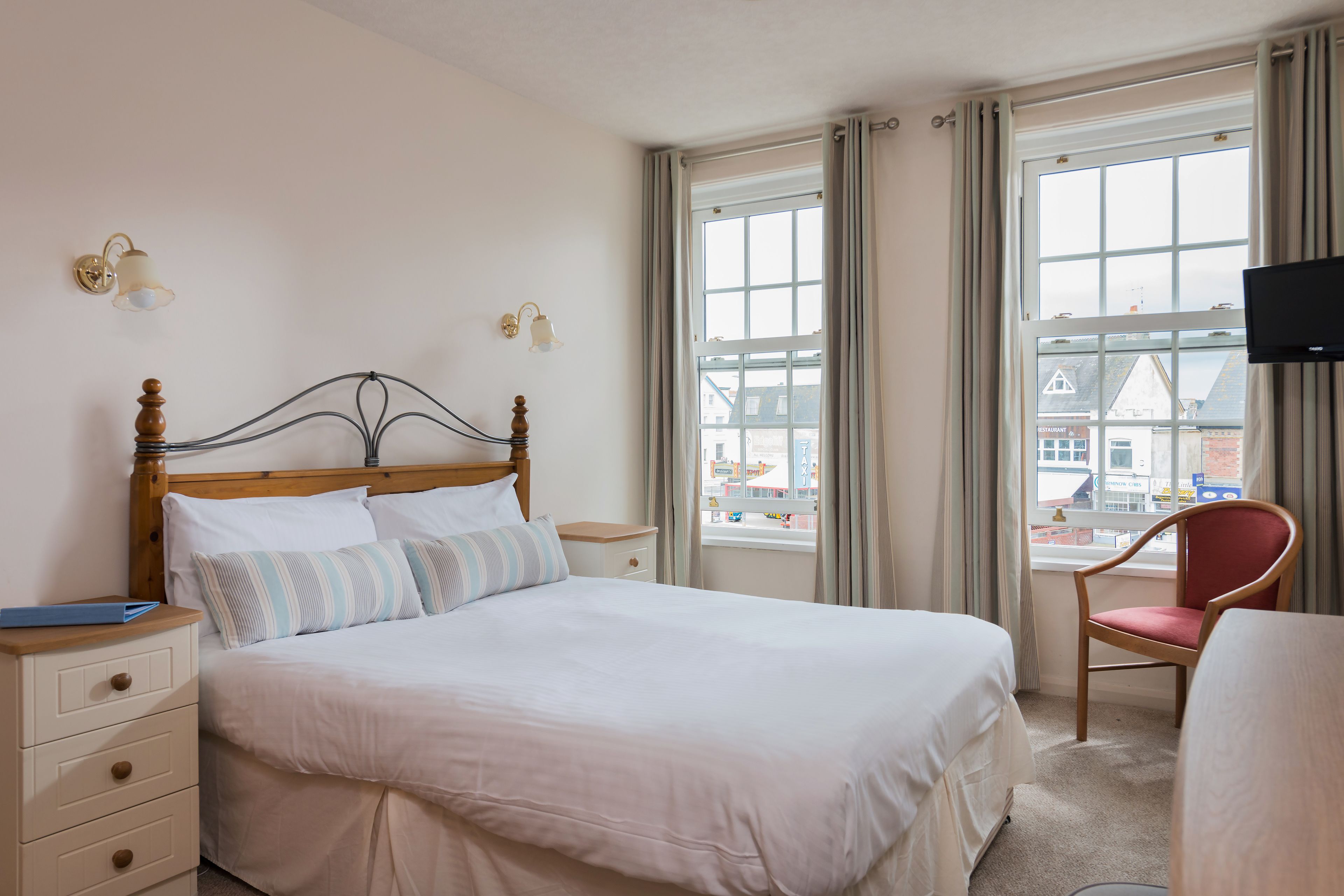 A hotel room with a large bed, a wooden headboard, two bedside tables, a chair, and a TV.