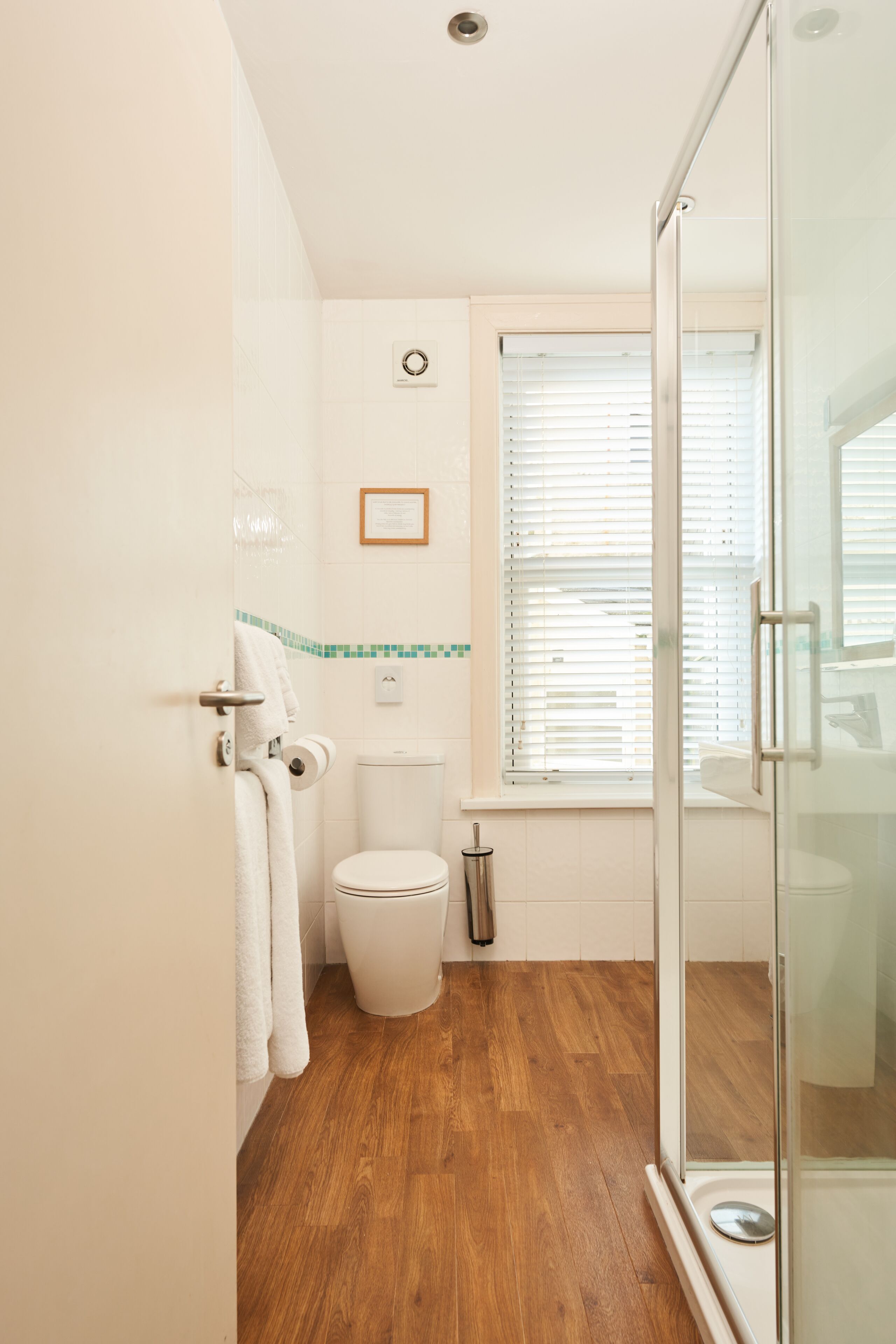 Un baño con inodoro, cabina de ducha de vidrio y ventana con persianas.