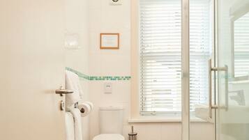 Un baño con inodoro, cabina de ducha de vidrio y ventana con persianas.