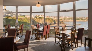 A restaurant with large windows offering a view of the coastline and buildings. - Great Western Hotel (Newquay)