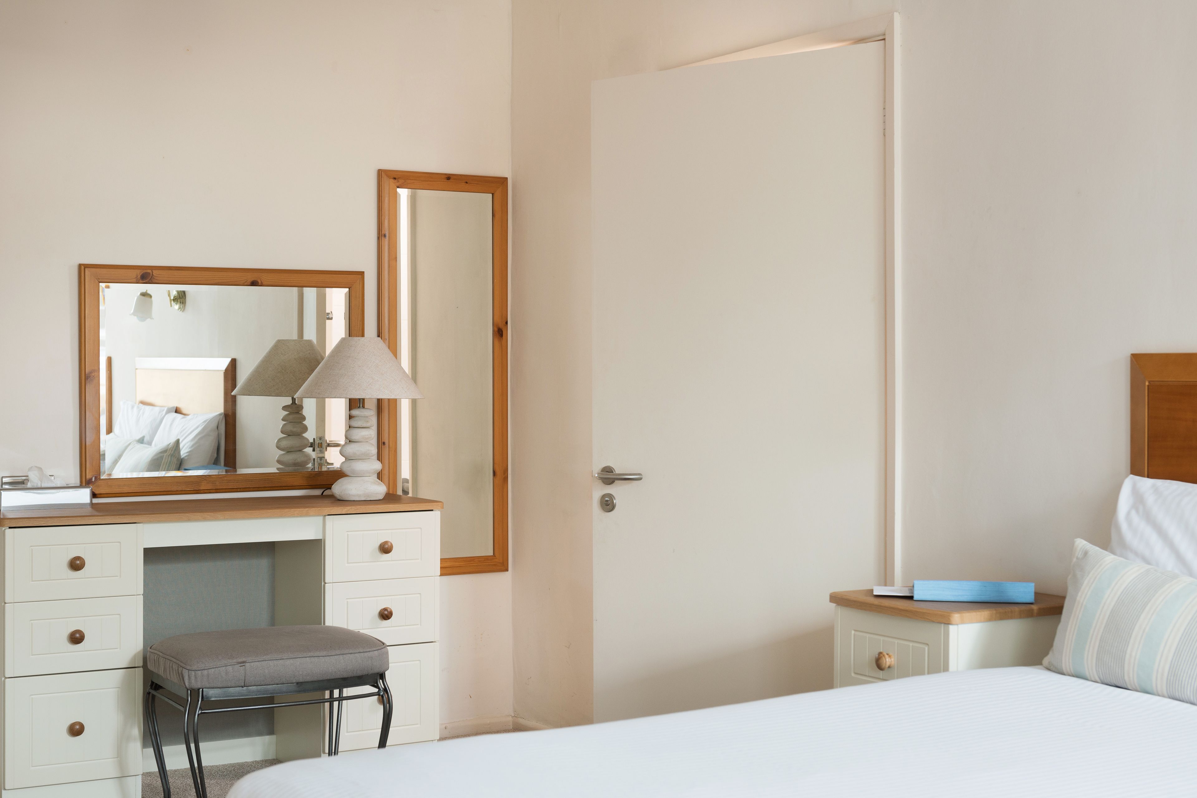 A bedroom with a bed, a bedside table, a nightstand, a dresser, a mirror, and a door.