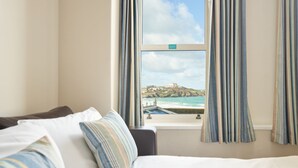 A hotel room with a bed, a window with curtains, and a view of a coastal landscape. - Great Western Hotel (Newquay)