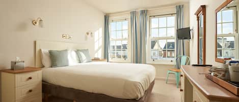 A bedroom with a bed, bedside tables, a dresser, a television, and large windows with curtains.