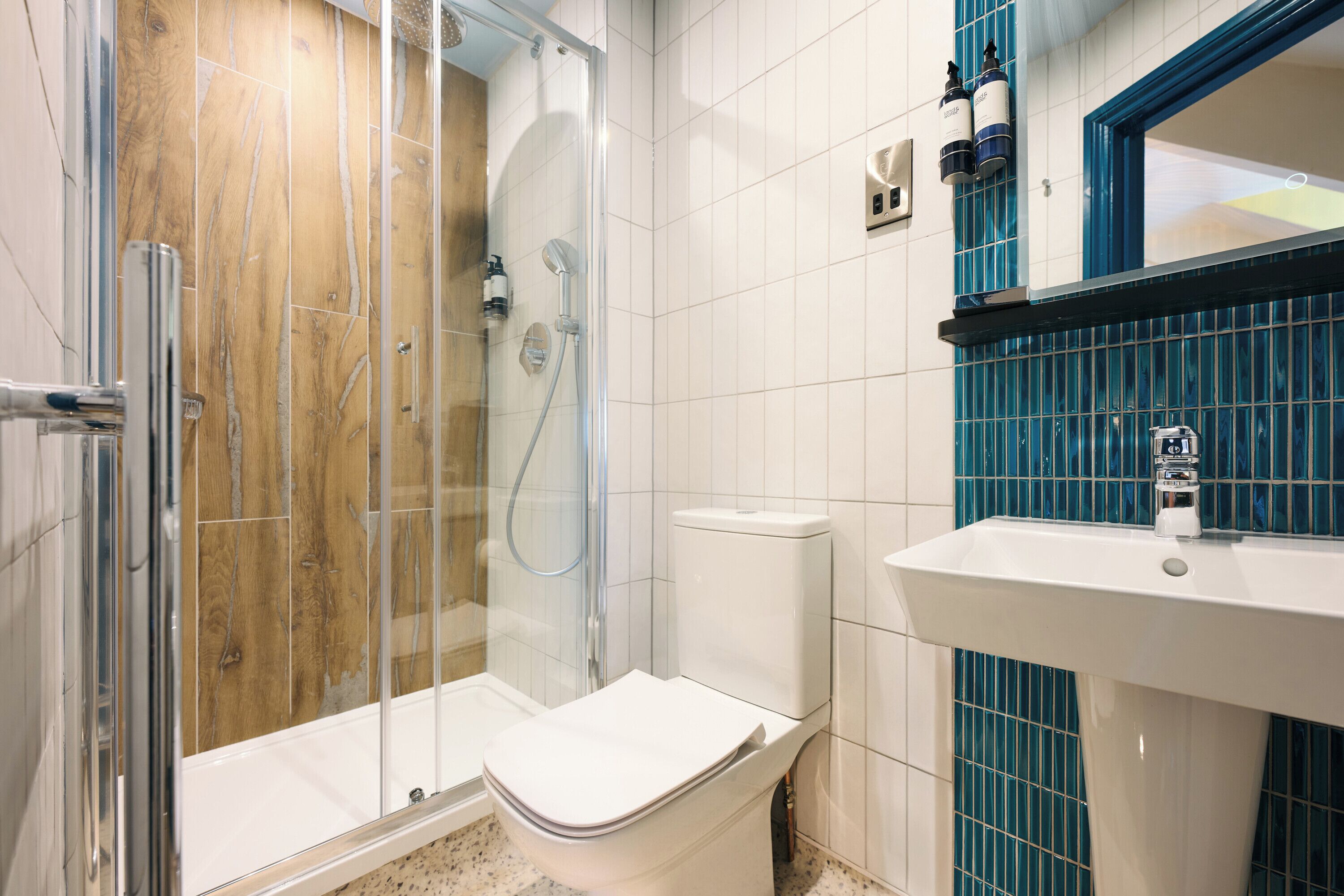A bathroom with a shower, toilet, sink, and blue-tiled wall.