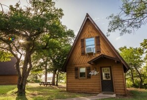 A small wooden cabin with a pitched roof, a window with shutters, and a door with a small sign. - Bay Landing RV Campground (Bridgeport)
