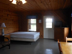 A wooden cabin room with a bed, a dresser, a television, and a window.