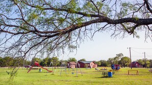 A playground with swings, slides, and a red building in the background.