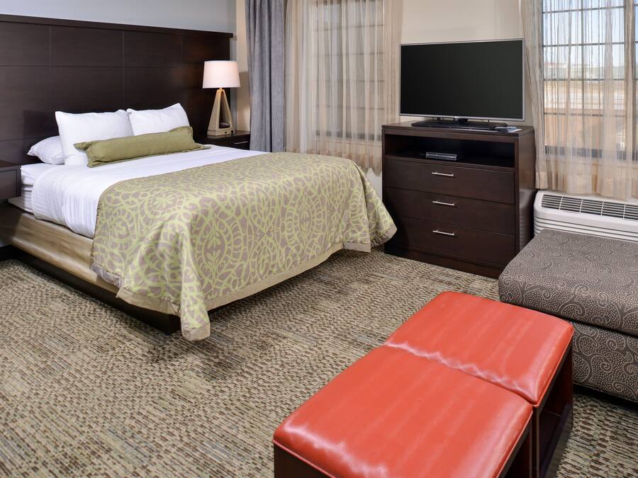 A hotel room with a bed, a TV, a desk, and a window with curtains.