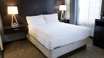 A hotel room with a large bed, two bedside tables with lamps, a dark headboard, and a view of the outdoors through sheer curtains.