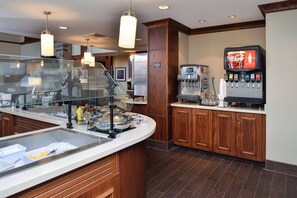 A self-service breakfast area with a refrigerator, beverage dispenser, and a glass display case. - Staybridge Suites Rochester - Commerce Dr NW by IHG (Rochester)