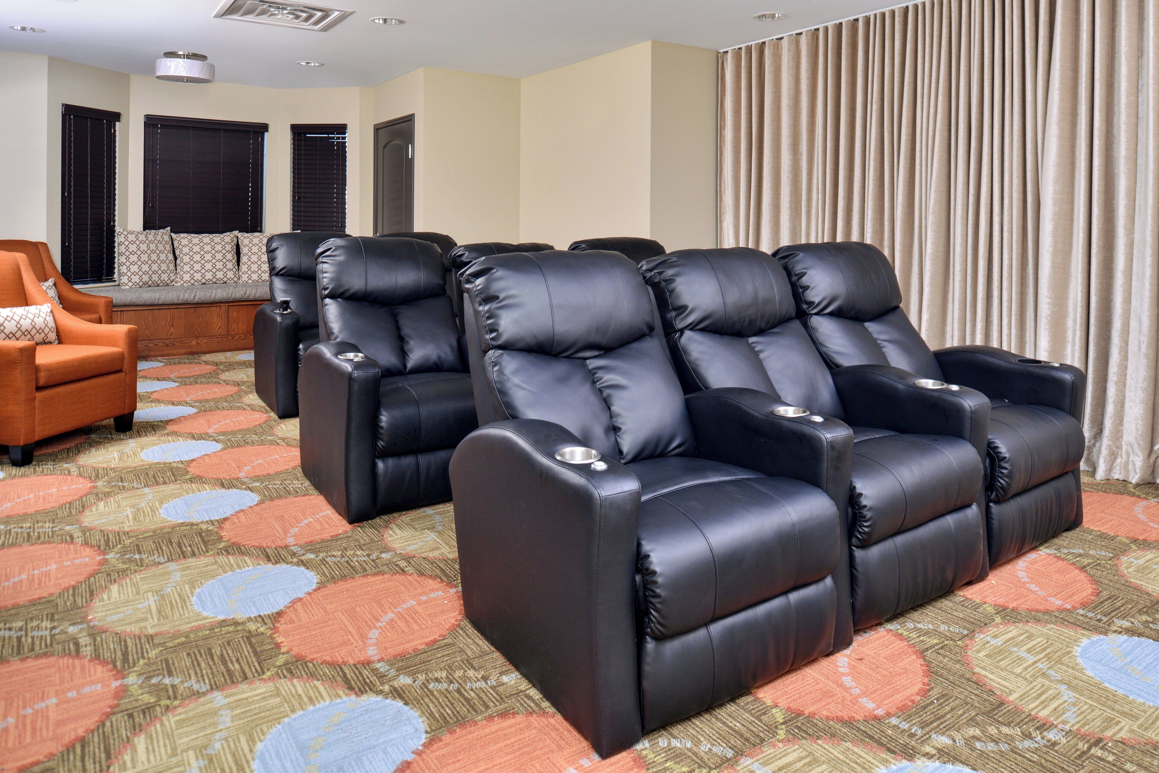 A room with a sofa, two black leather recliners, a patterned carpet, and a window with blinds.