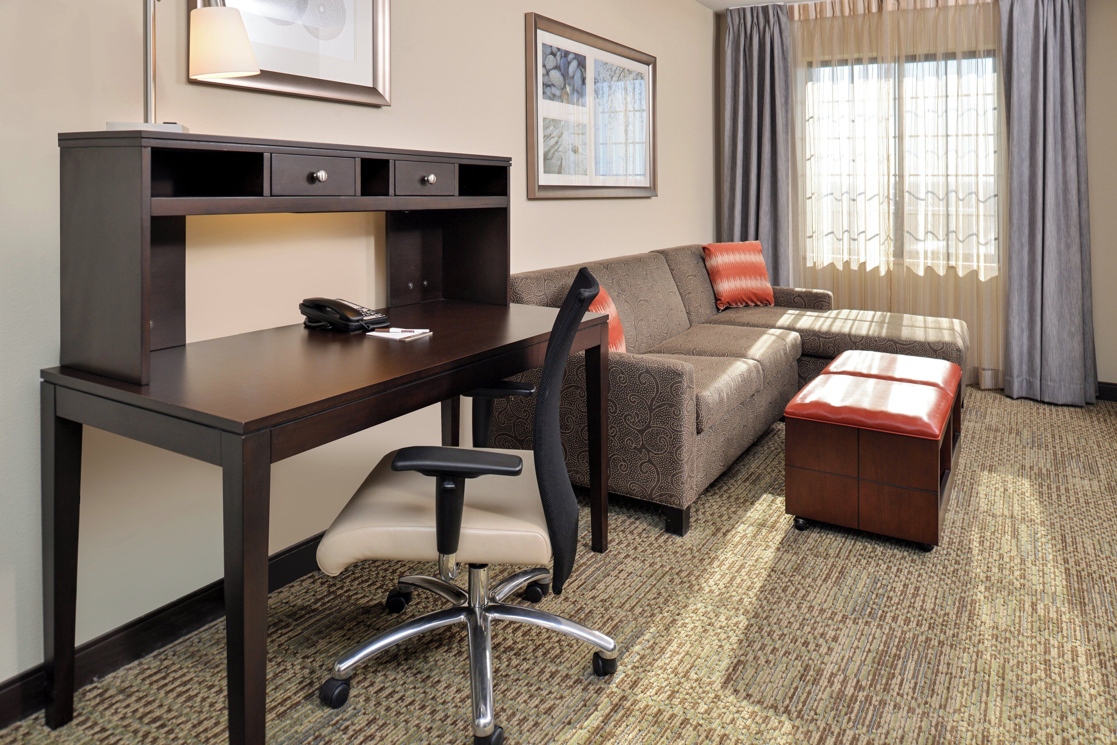 A hotel room with a desk, chair, sofa, and ottoman.