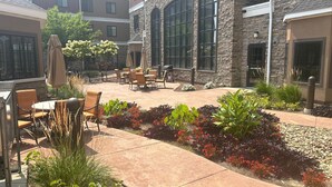An outdoor patio area with stone walls, outdoor seating, and landscaped gardens. - Staybridge Suites Rochester - Commerce Dr NW by IHG (Rochester)