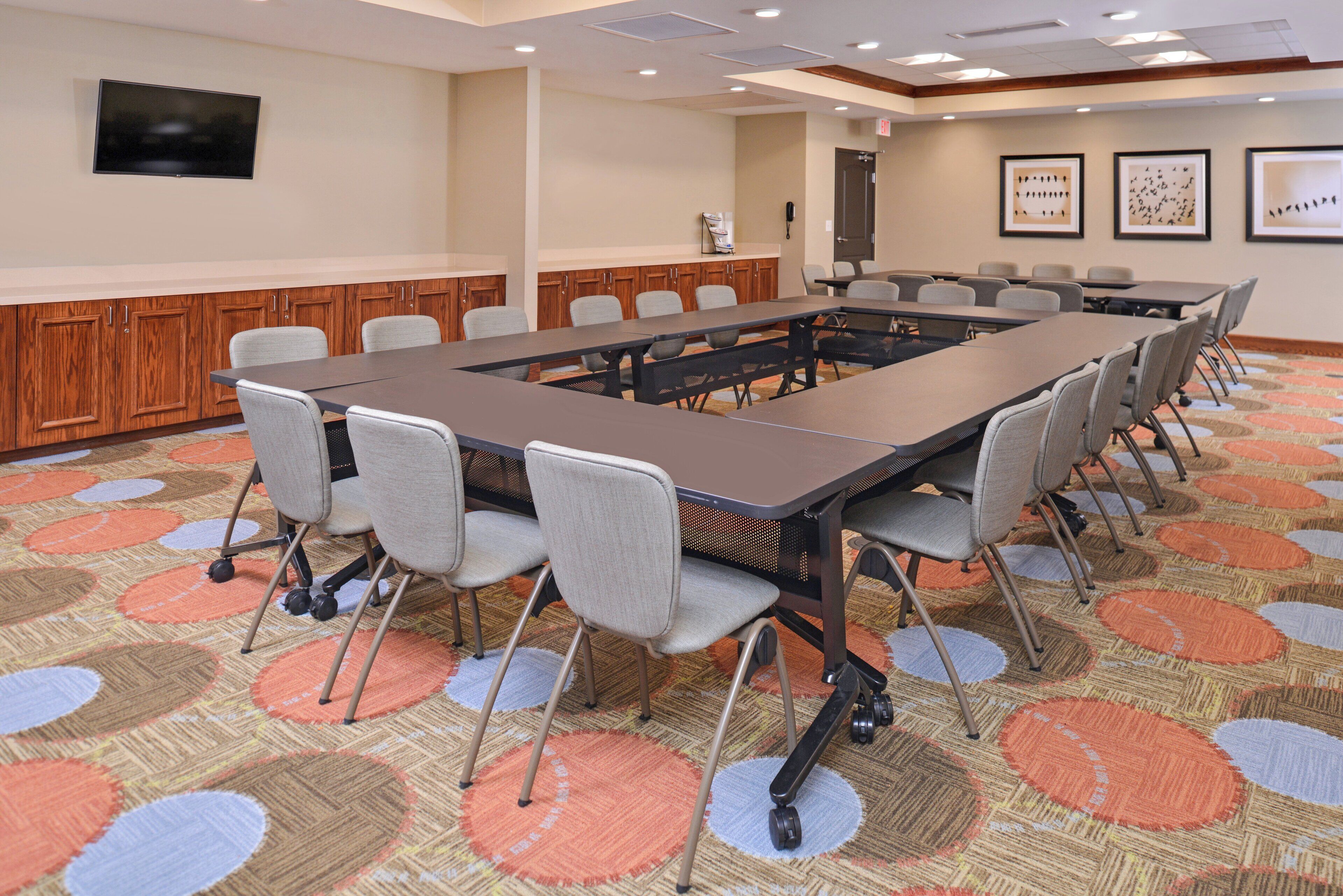 A conference room with a long table, chairs, a television, and framed pictures on the wall.