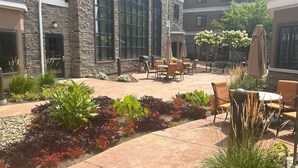 A courtyard with outdoor seating, stone walls, and various plants. - Staybridge Suites Rochester - Commerce Dr NW by IHG (Rochester)