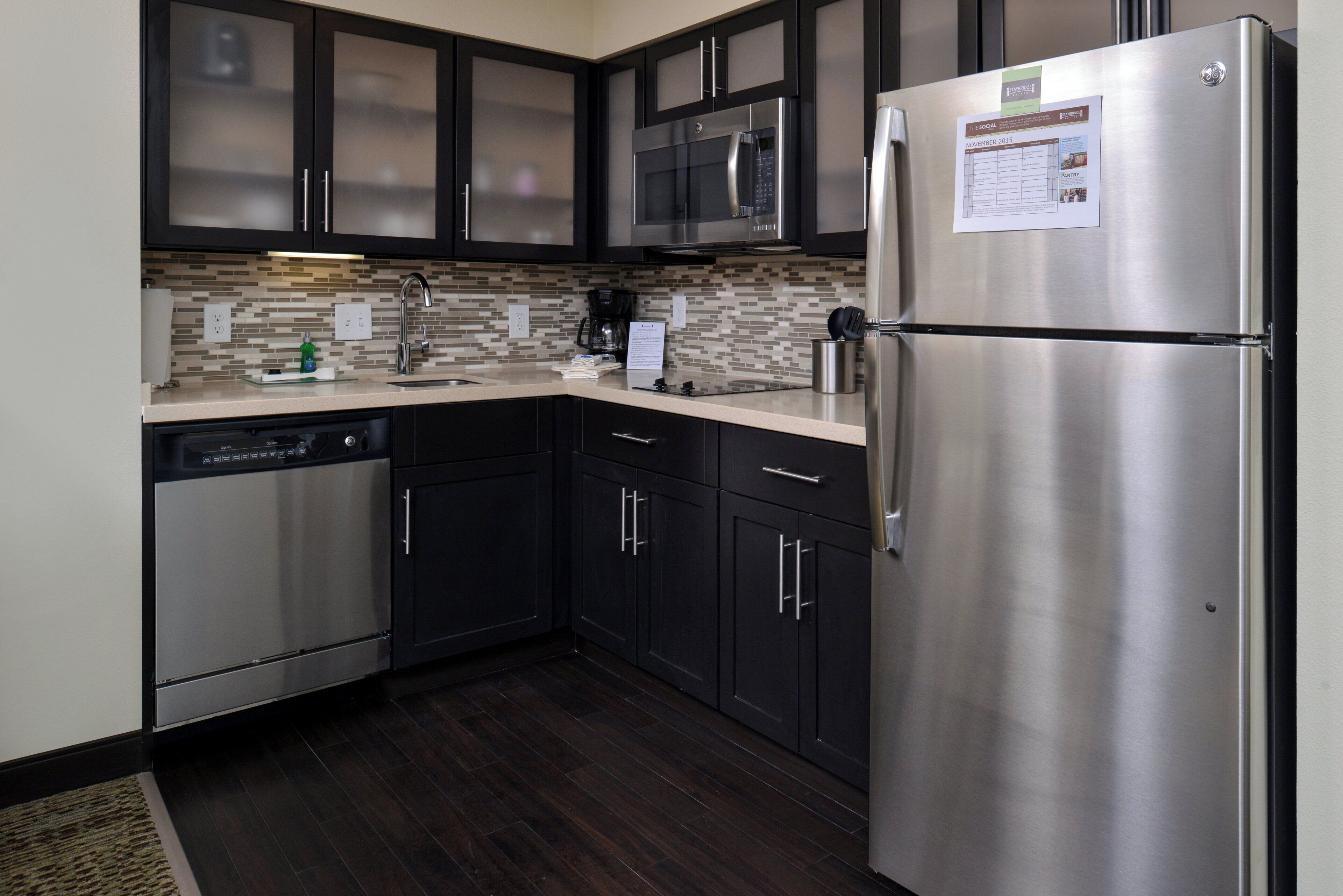 A modern kitchen with stainless steel appliances, dark cabinetry, and a tiled backsplash.