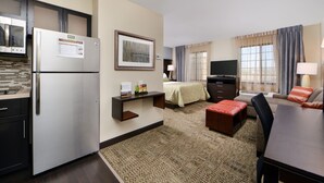A compact hotel room with a kitchenette, a bed, a TV, and a seating area. - Staybridge Suites Rochester - Commerce Dr NW by IHG (Rochester)