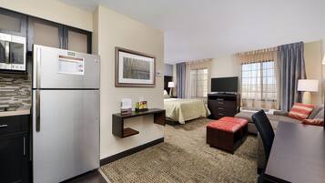 Habitación de hotel compacta con kitchenette, cama, televisor y zona de estar.