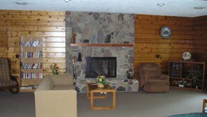 Una sala de estar acogedora con chimenea de piedra, paredes de madera, una estantería y un sofá cómodo.