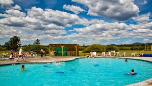 Une piscine où des personnes se baignent et profitent de l’eau, entourée d’un espace de repos couvert et de verdure.