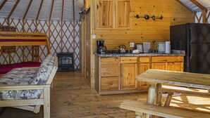 Un intérieur chaleureux avec un banc en bois, un coin cuisine doté de meubles en bois et d’un réfrigérateur, ainsi qu’une table à manger.