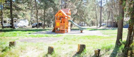 Un parque infantil con un tobogán y una casita de juegos en un área boscosa.