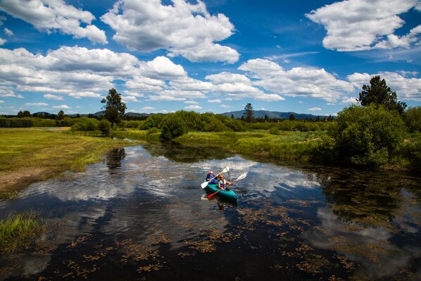 A river with kayaks, surrounded by greenery and a clear sky.