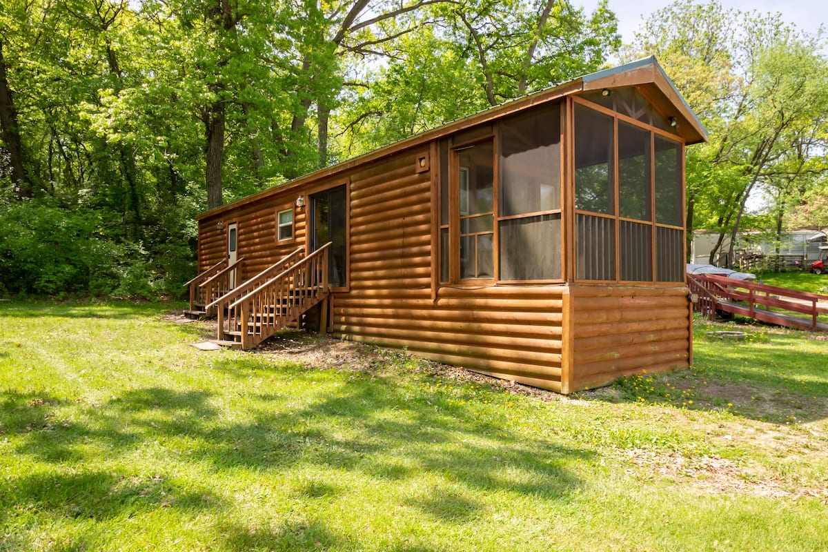 A wooden cabin with a large window, a staircase leading to the entrance, and a small porch area.