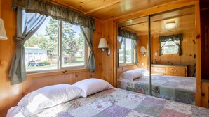 A wooden cabin room with two beds, a dresser, and a window with curtains. - Blackhawk RV Campground (Milton)