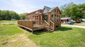 A wooden cabin with a deck, large windows, and a green roof. - Blackhawk RV Campground (Milton)
