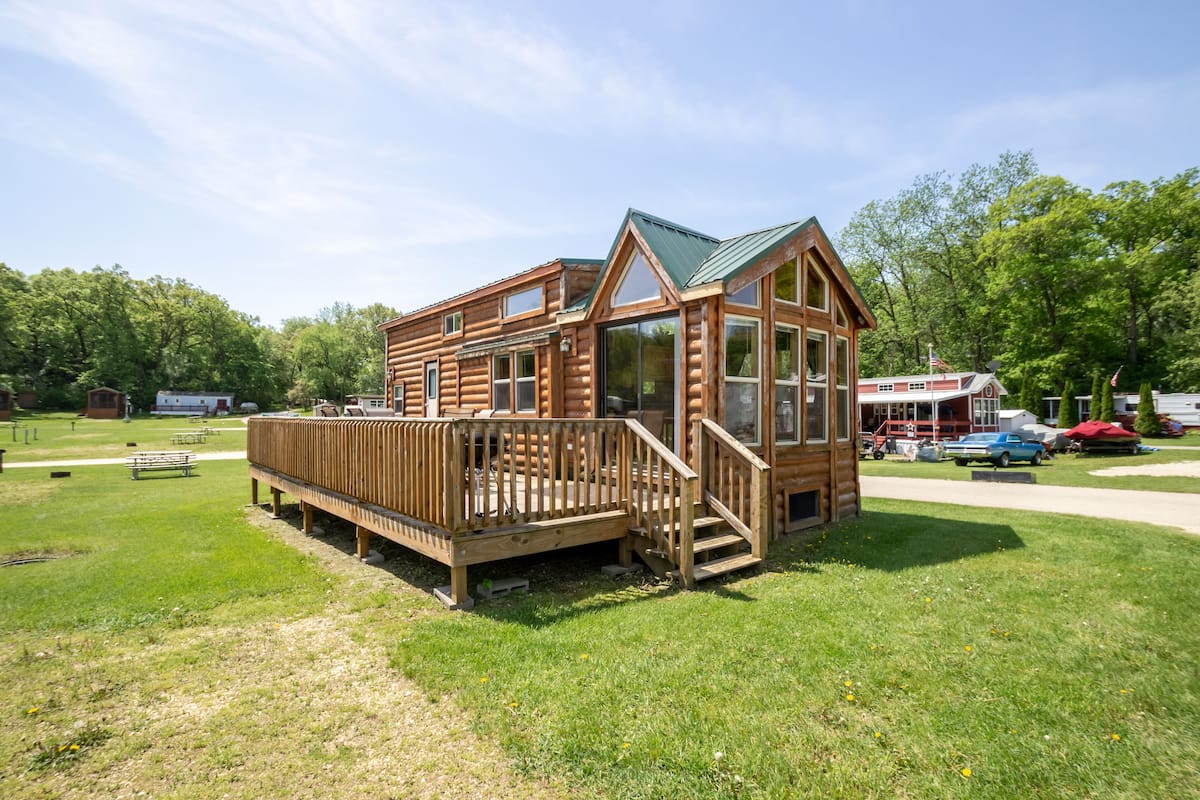 A wooden cabin with a deck, large windows, and a green roof.