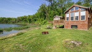 A wooden cabin with a deck, a picnic table, and a fire pit by a lake. - Blackhawk RV Campground (Milton)