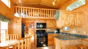 A wooden cabin interior with a kitchen featuring a stove, microwave, and bar stools. - Blackhawk RV Campground (Milton)