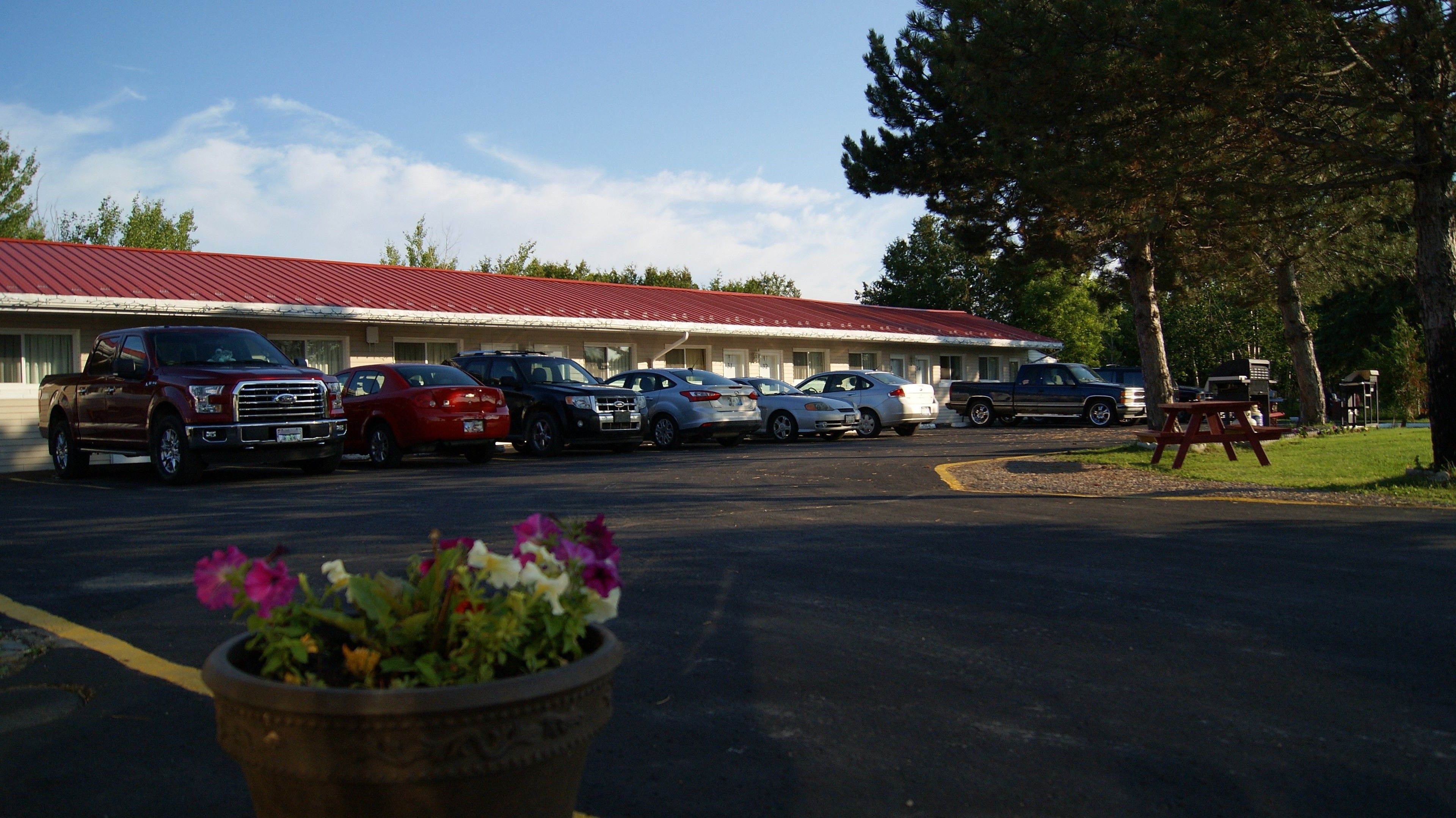 A motel with a red roof and several parked cars in the driveway.