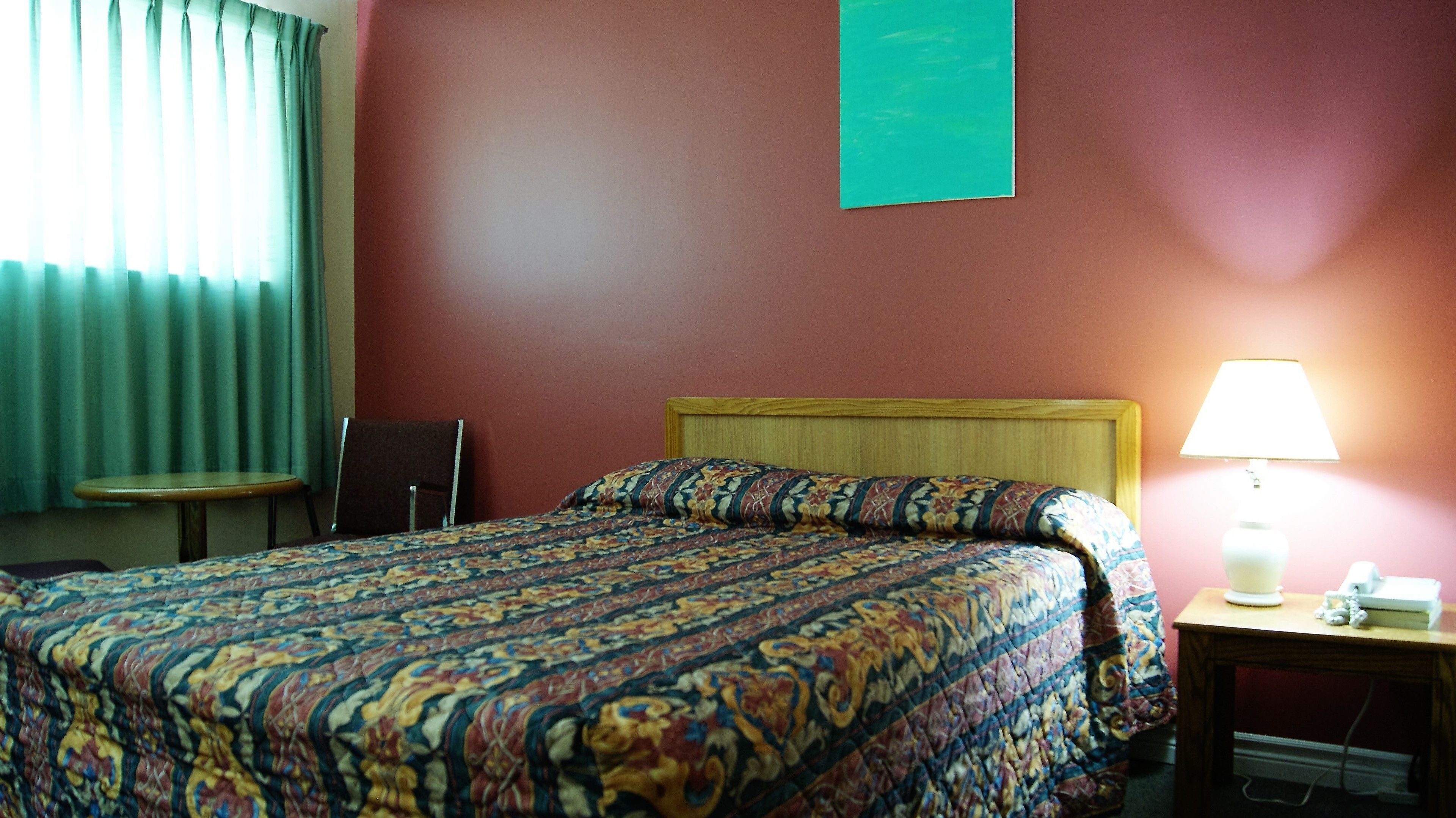 Habitación de hotel con cama, mesita de noche con lámpara, una silla y ventana con cortinas.