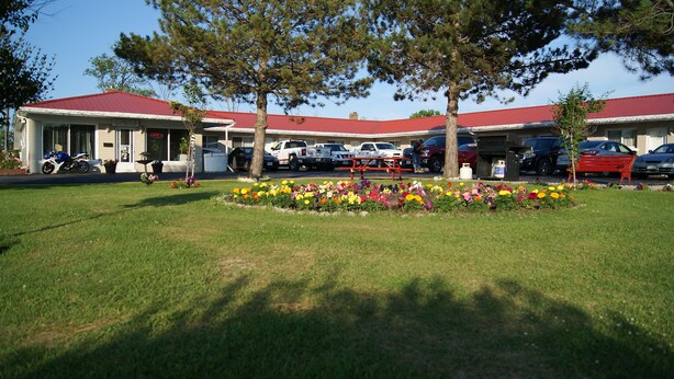 Un motel con techo rojo, varios espacios de estacionamiento y un jardín frontal.