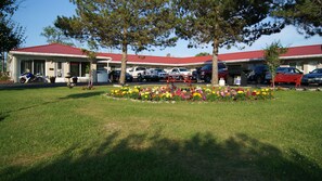 Un motel avec un toit rouge, plusieurs places de stationnement et un parterre de fleurs à l’avant.