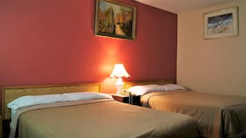 A hotel room with two beds, a nightstand with a lamp, and two framed pictures on the wall.