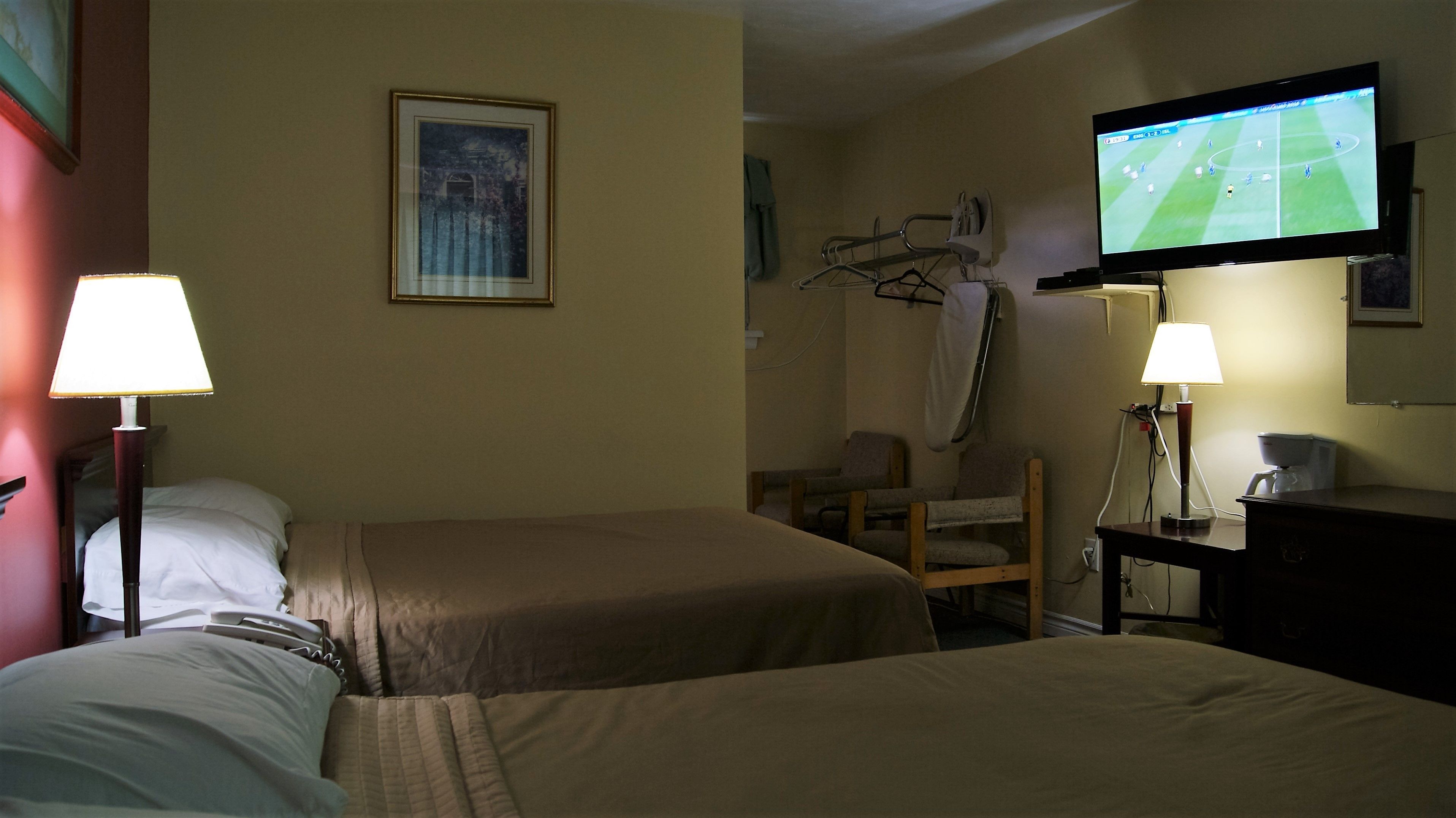 Habitación de hotel con dos camas, un televisor en la pared, una silla y un escritorio con una lámpara.