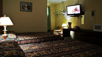 A hotel room with a bed, a TV, a desk with a lamp, and a chair.