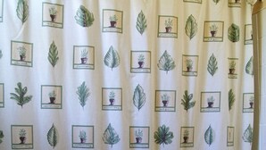Un baño con cortina de ducha estampada con motivos vegetales, una bañera y un lavamanos blanco.