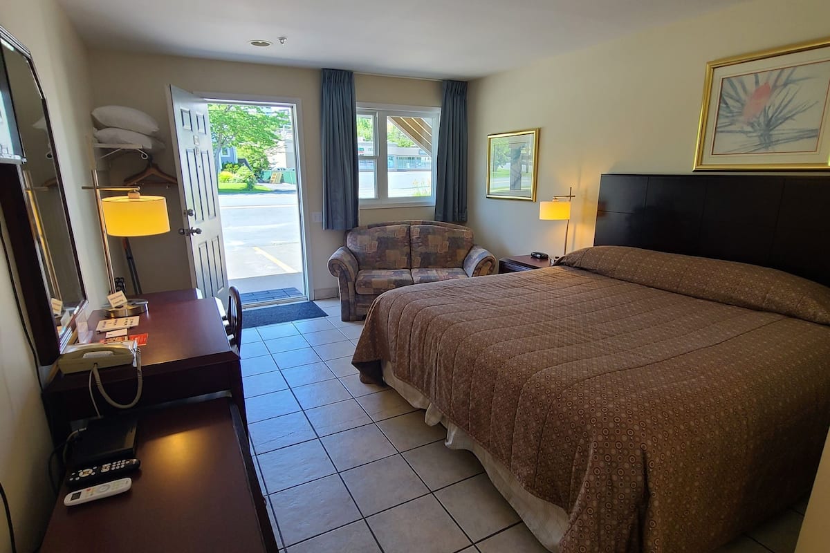 A hotel room with a bed, a desk with a telephone, a chair, and a window with curtains.