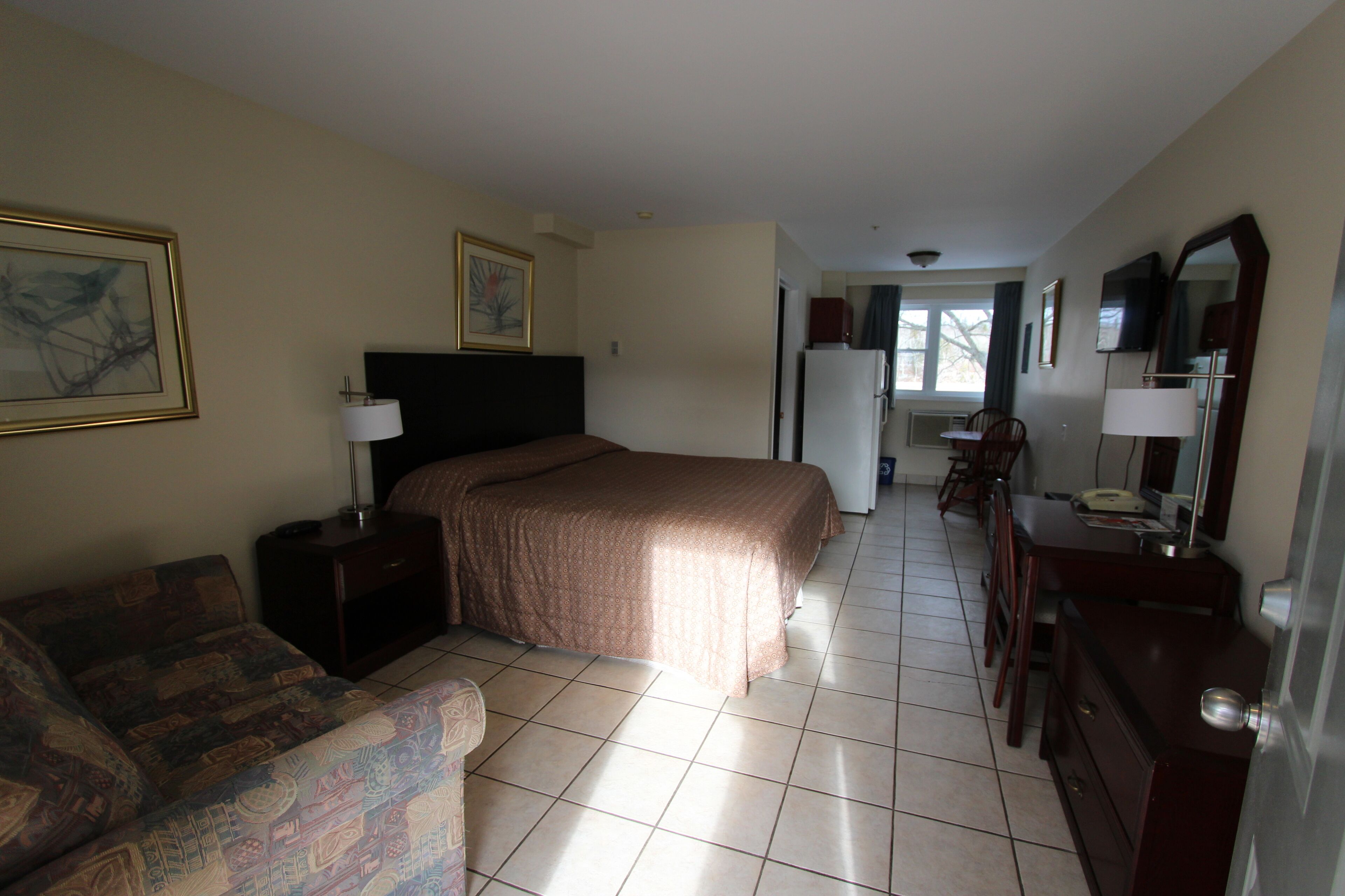 Una habitación de hotel con cama, escritorio, silla, cómoda y televisión.
