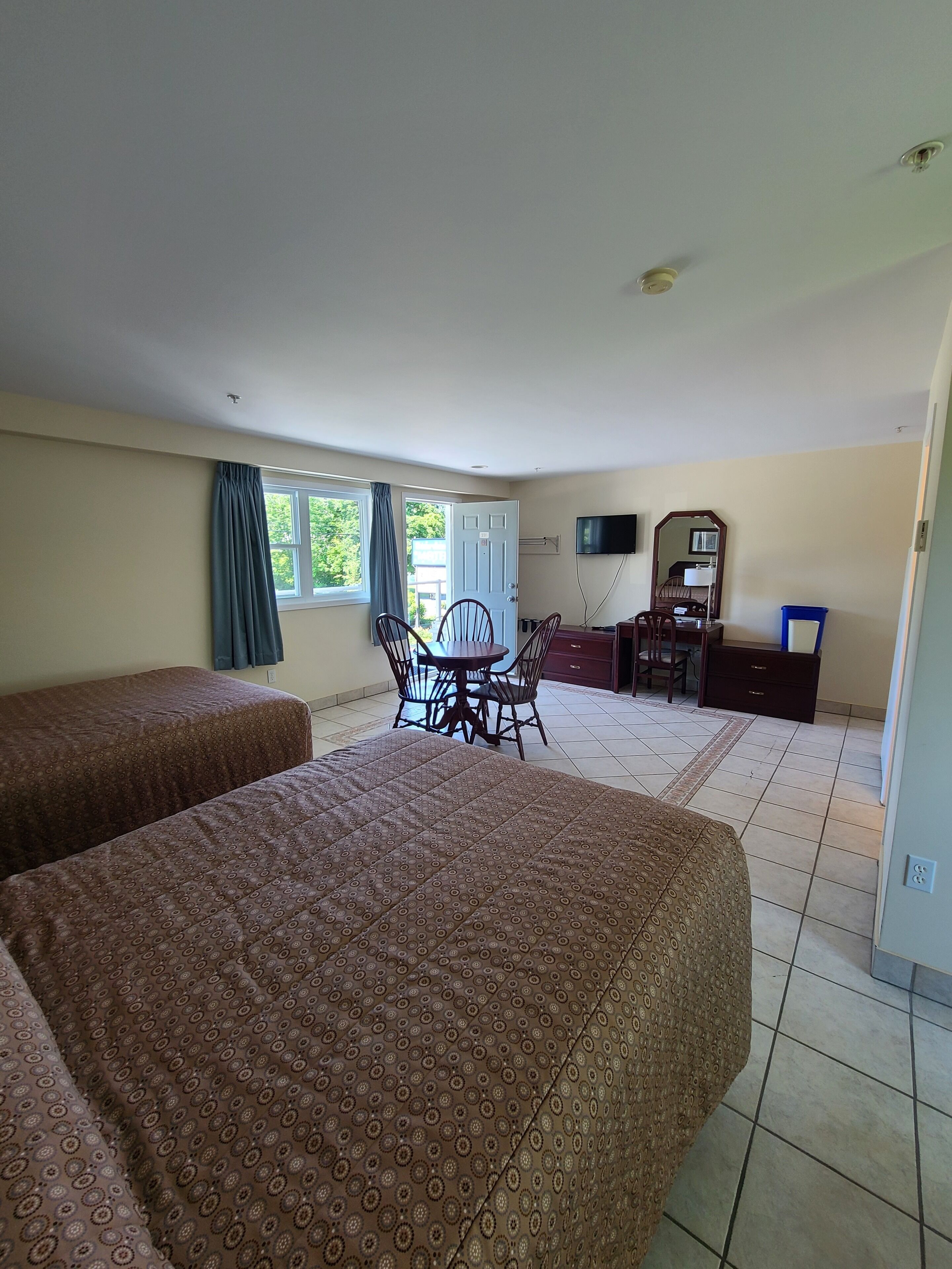 A hotel room with two beds, a dining table with chairs, a TV, a dresser, and a window with curtains.